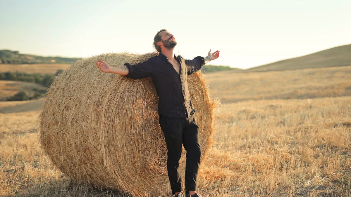 Man enjoying the summer sun while leaning on a hay bale in a rural field.